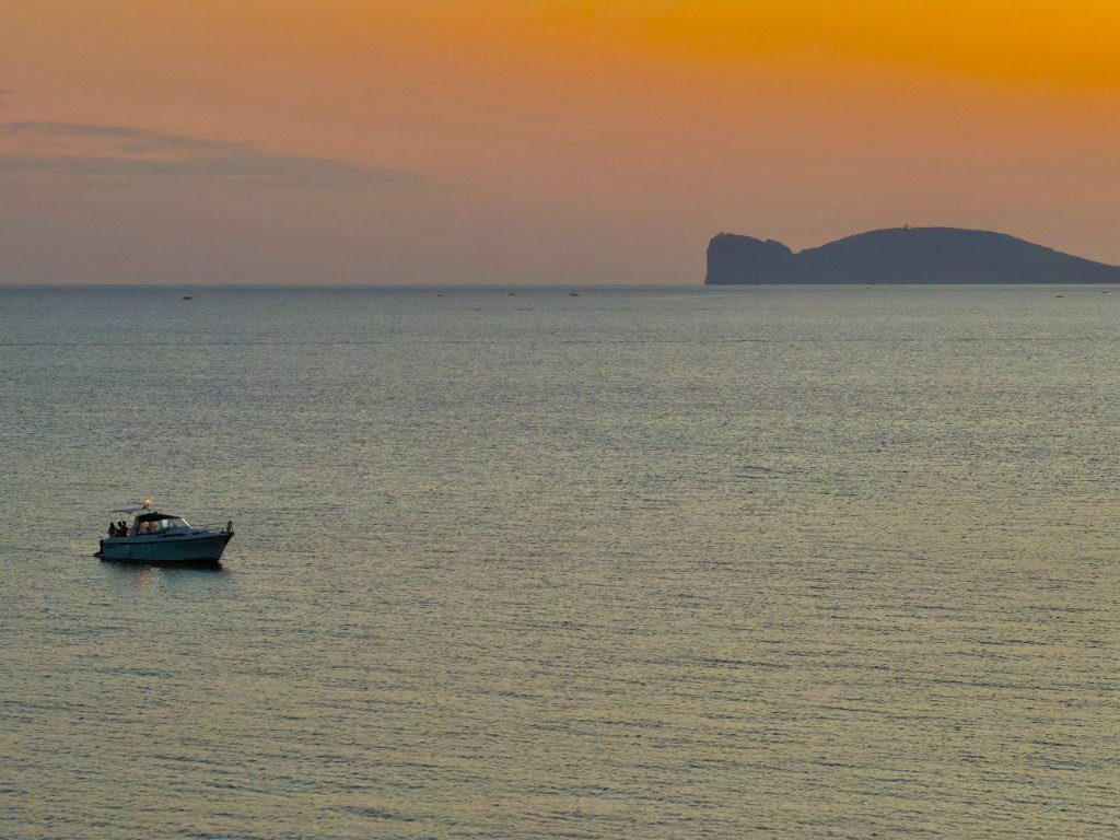 Barca a vela al tramonto davanti alla costa di Alghero